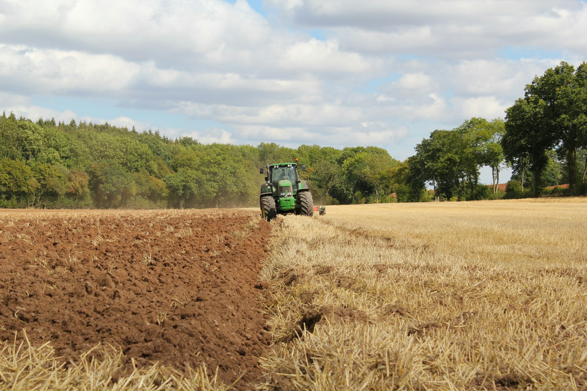 Fruchtbares Ackerland das gerade mit einem John Deere Traktor gepflügt wird.